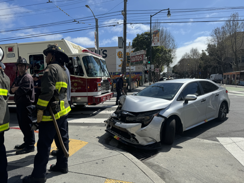 A crashed silver sedan next to a fire truck and firefighters